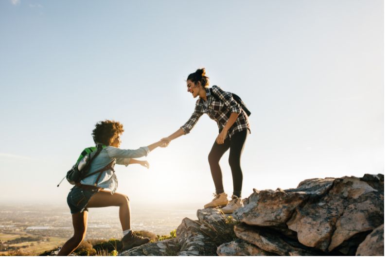woman helping her friend climb mountain with clasped hands